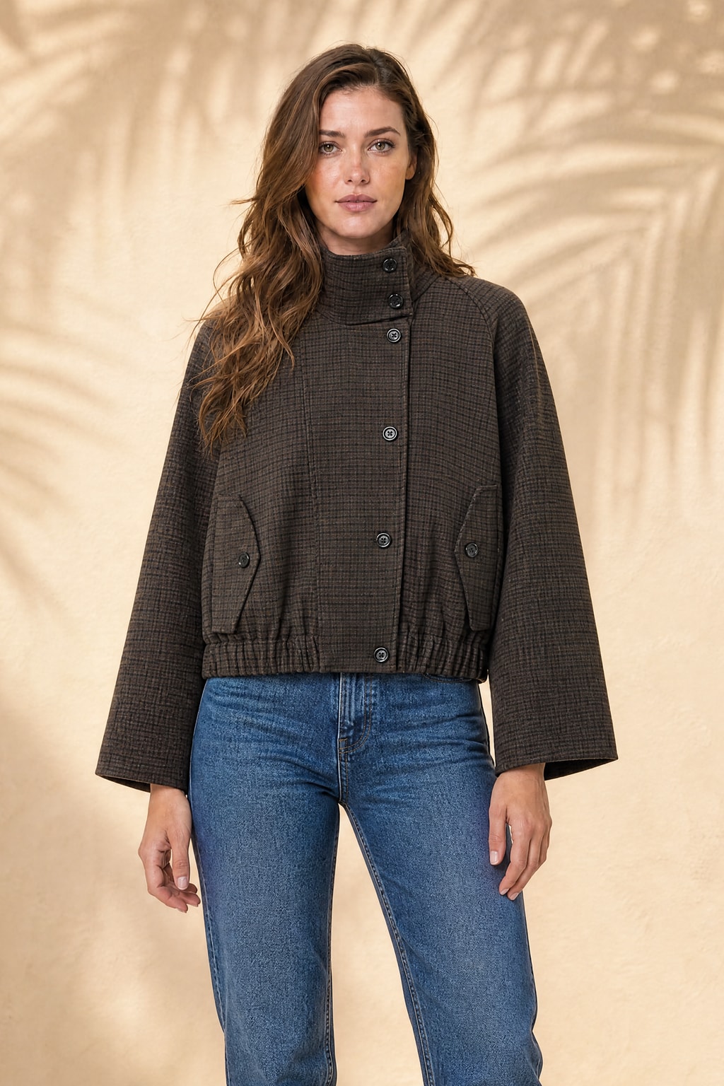 Chocolate checked funnel-neck jacket over blue jeans on a model against a warm plaster wall — generated studio photo