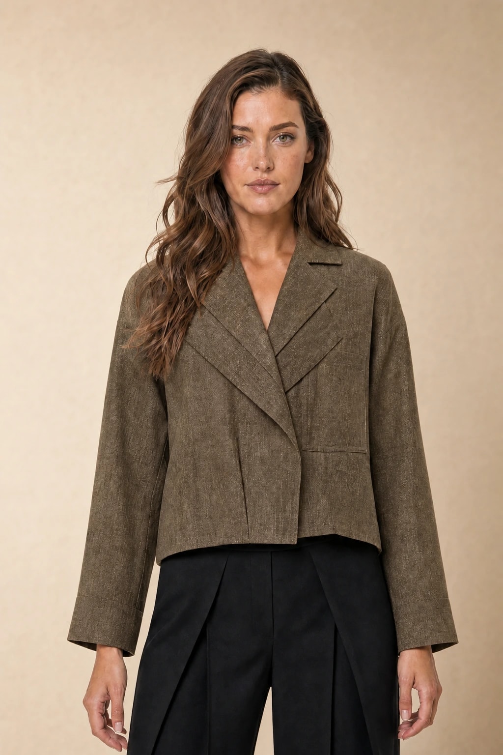 Oversized olive linen jacket with wide notched lapels over black trousers on a model against a warm beige studio backdrop — generated studio photo